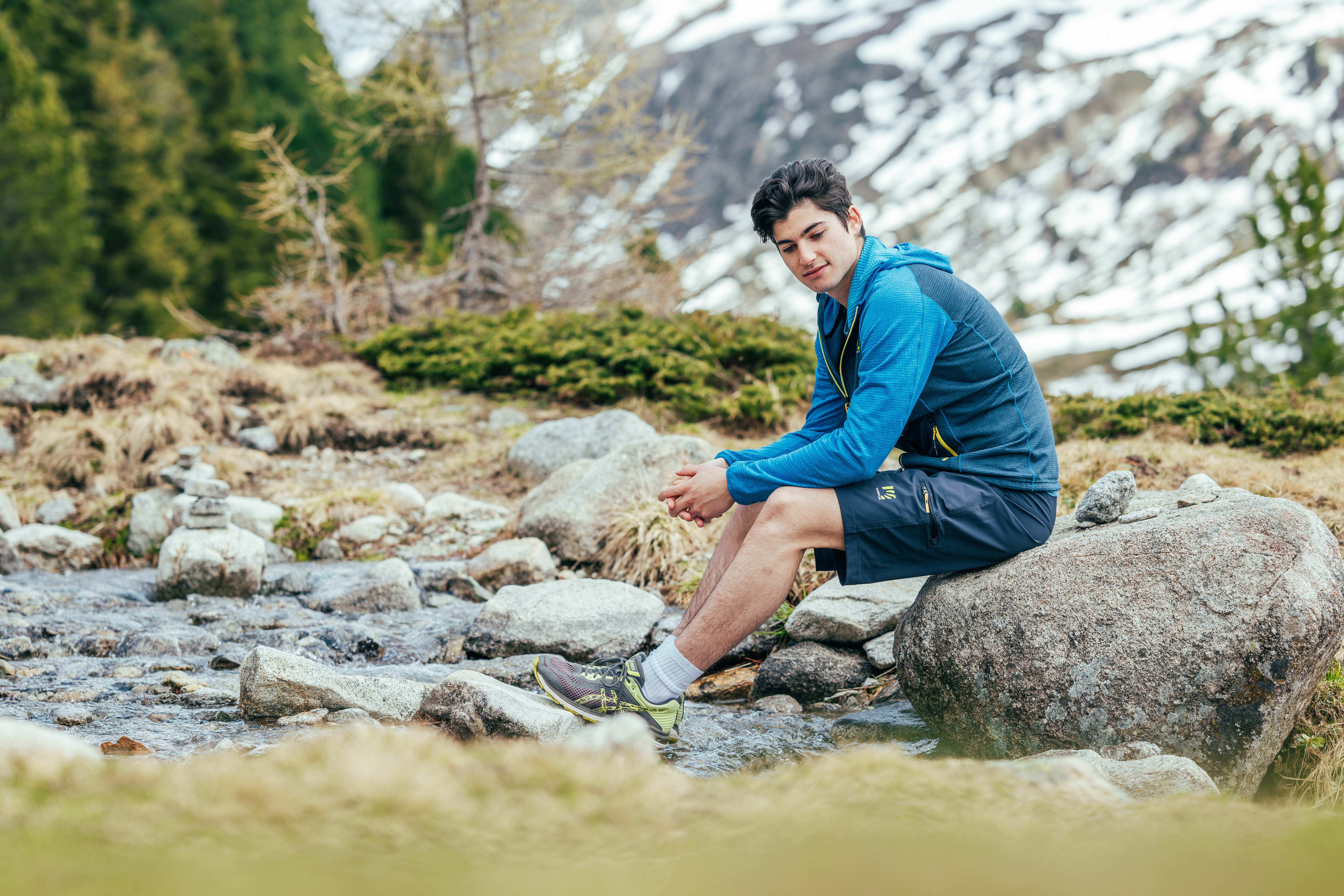 Wanderer bindet seinen Schuh vor einer Bergkulisse