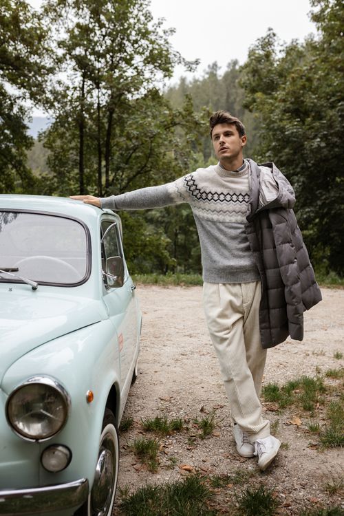 Mann mit Strickpullover und Steppjacke neben einem Auto